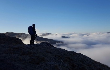 Mountaineer silhouetted against blue sky above cloud inversion