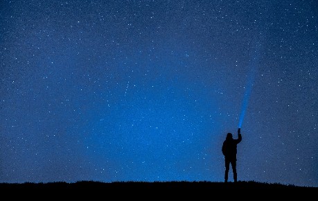 Man shining torch into star-filled sky